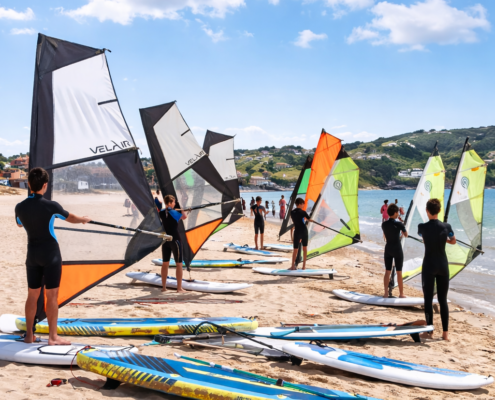 Niños en viaje de fin de curso con su centro escolar en la playa practicando windsurf